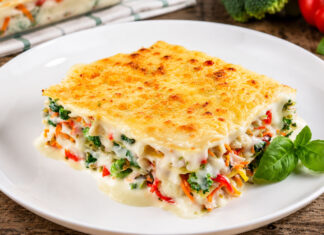 Lasanha de Bacalhau e Legumes Fatia de lasanha de bacalhau e legumes com molho bechamel cremoso e cobertura gratinada dourada, servida num prato branco, uma receita reconfortante e perfeita para um almoço ou jantar em família.